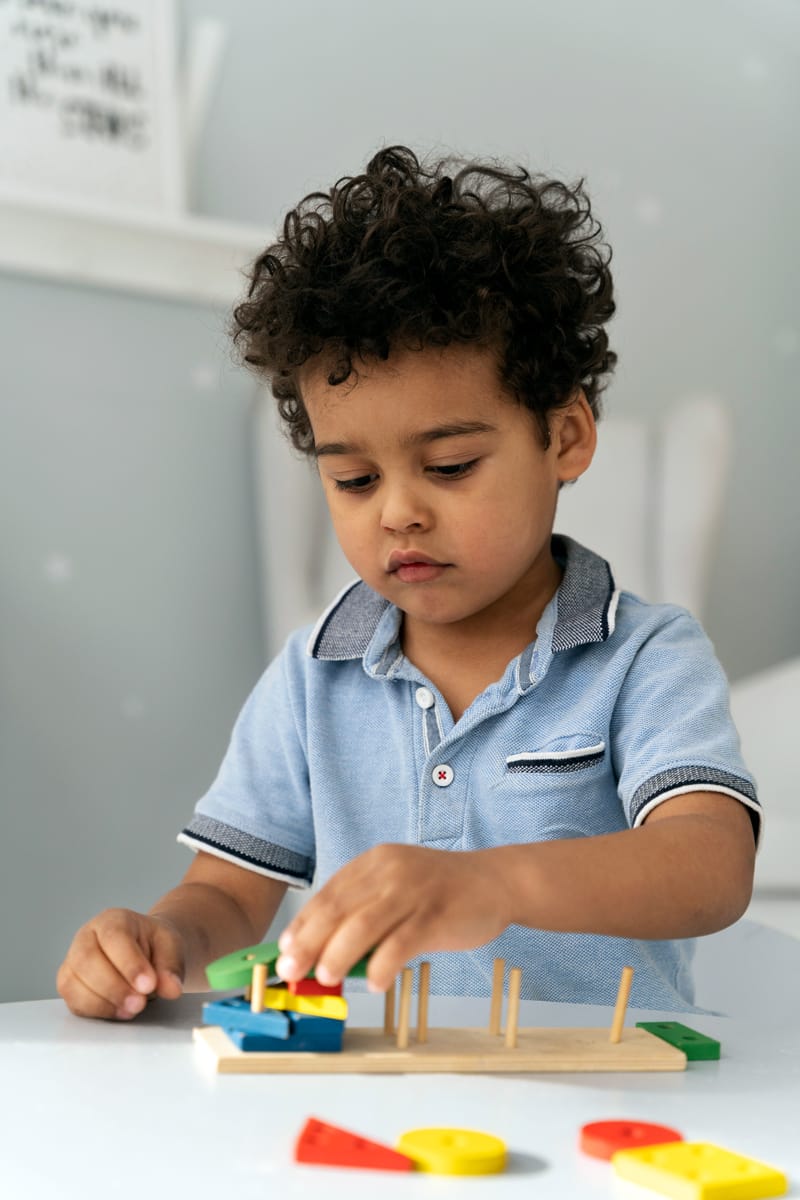 young boy sat at a table playing with a wooden block game