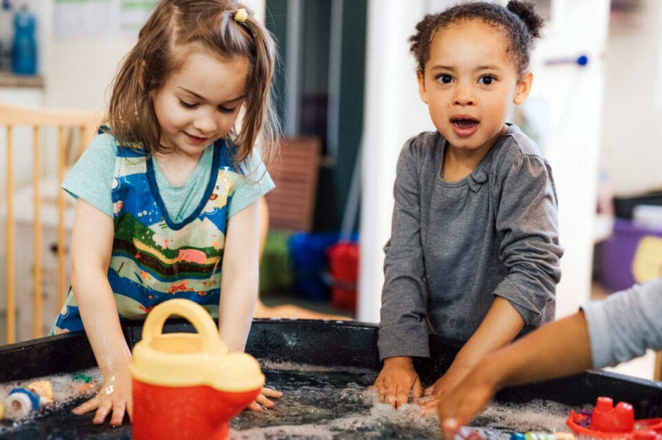 Two girls playing with their hands in a large trough of water
