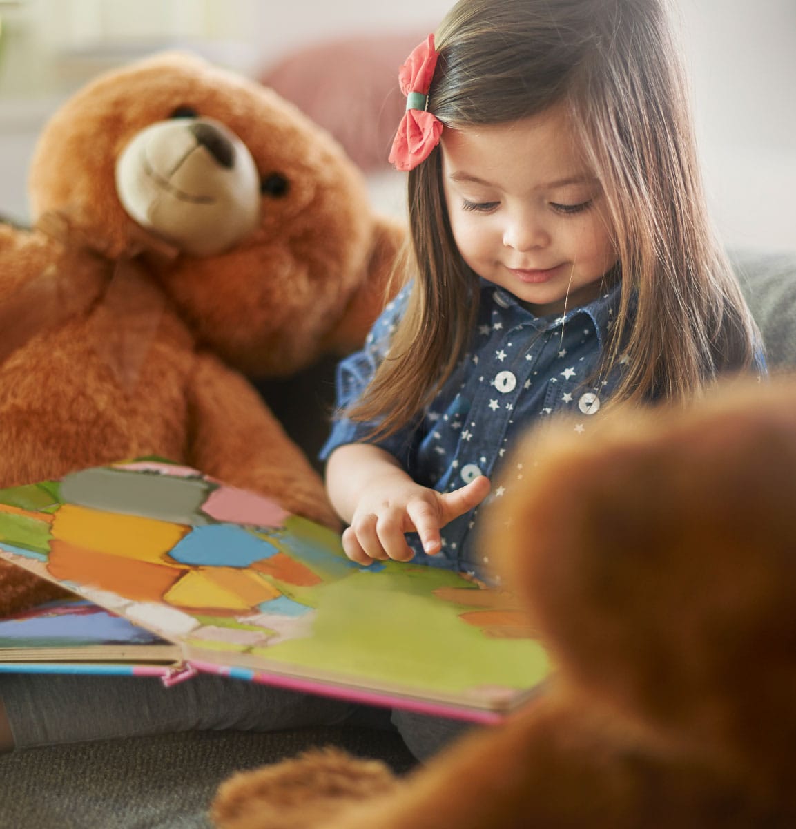 little girl reading a book with her teddy bears